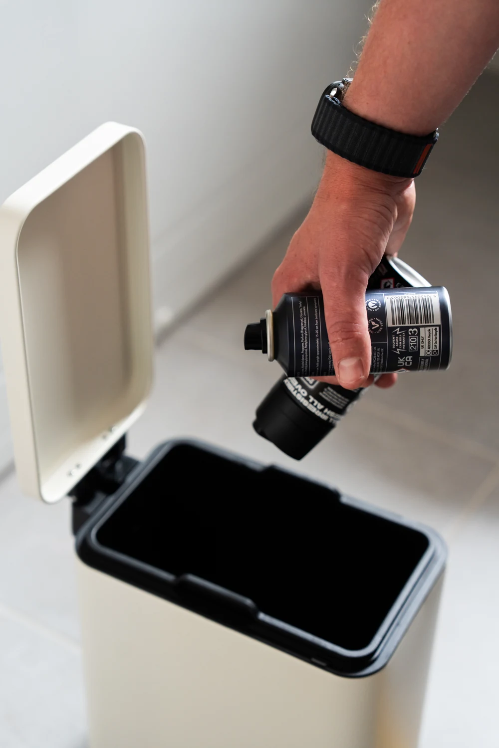 A person holding two aerosol cans above an open household bin.