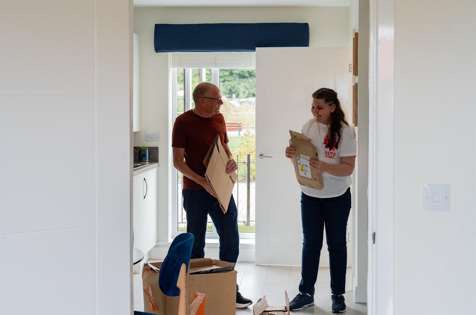 A man and girl holding flattened cardboard and paper packaging together at home.